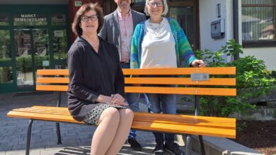 Frau sitzt auf oranger Bank, der Bürgermeister der Gemeinde Kirchbach und eine weitere Frau stehen dahinter. (c) Gemeinde Kirchbach